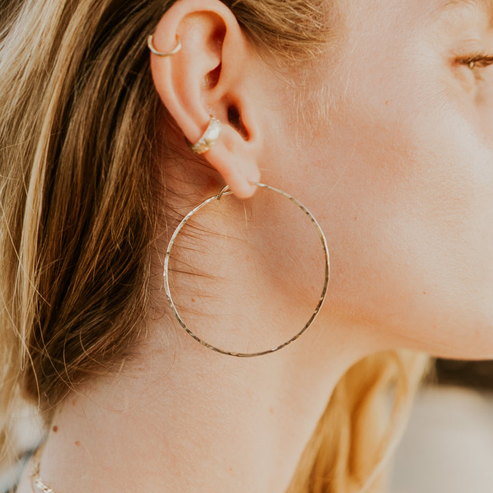 Close-up of a person wearing gold hoop earrings with a blurred background