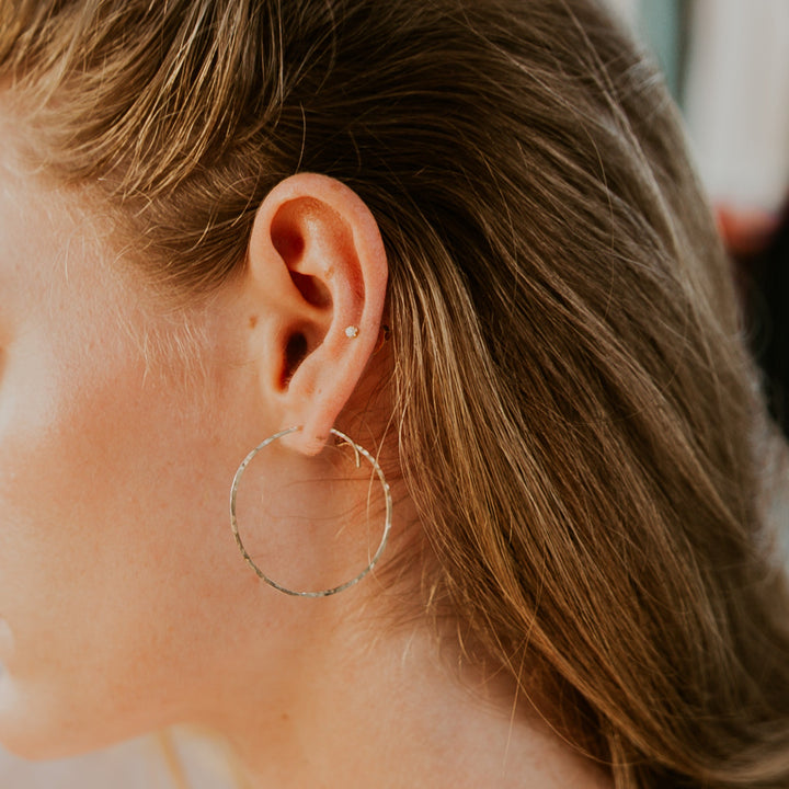 Close-up of an ear wearing a gold hoop earring with blurred background