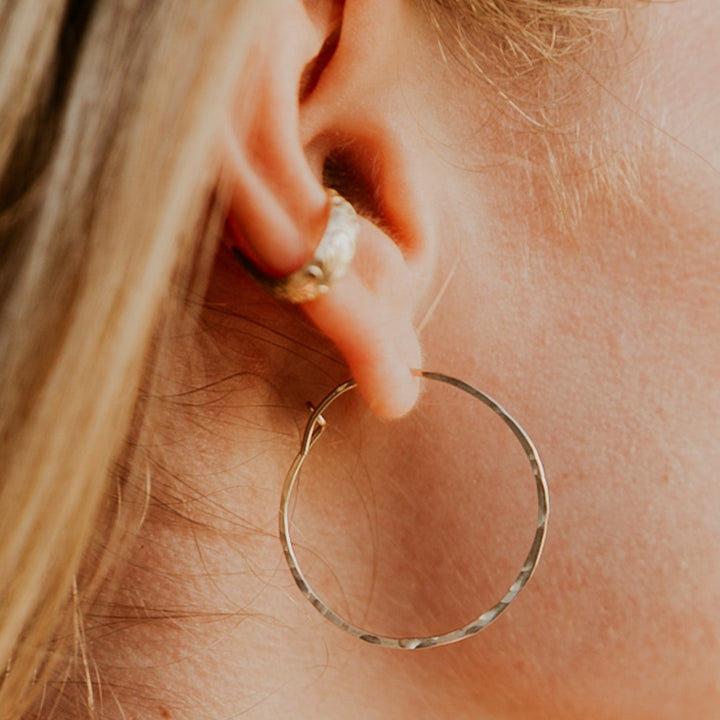 Close-up of a person wearing a gold hoop earring with a blurred background