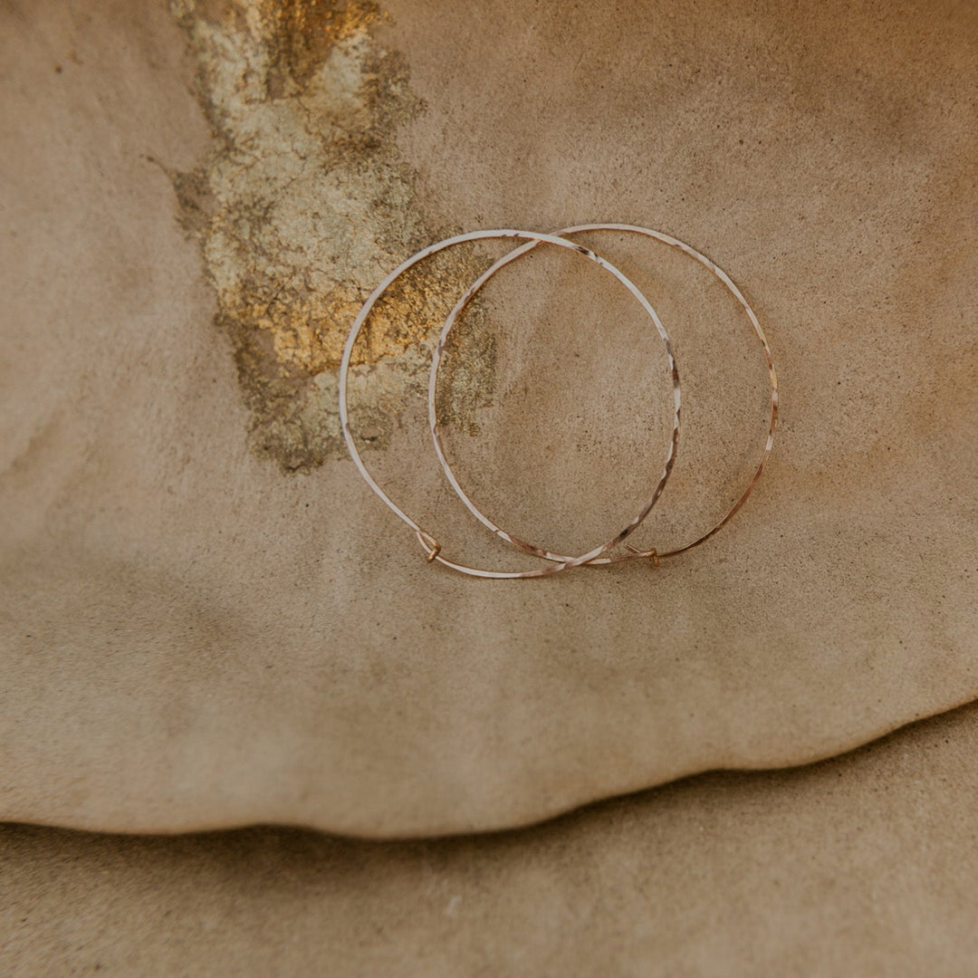 Two gold hoop earrings on a textured brown surface