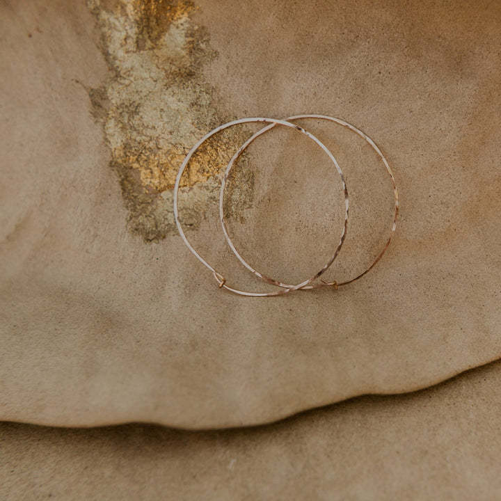 Two gold hoop earrings on a textured brown surface