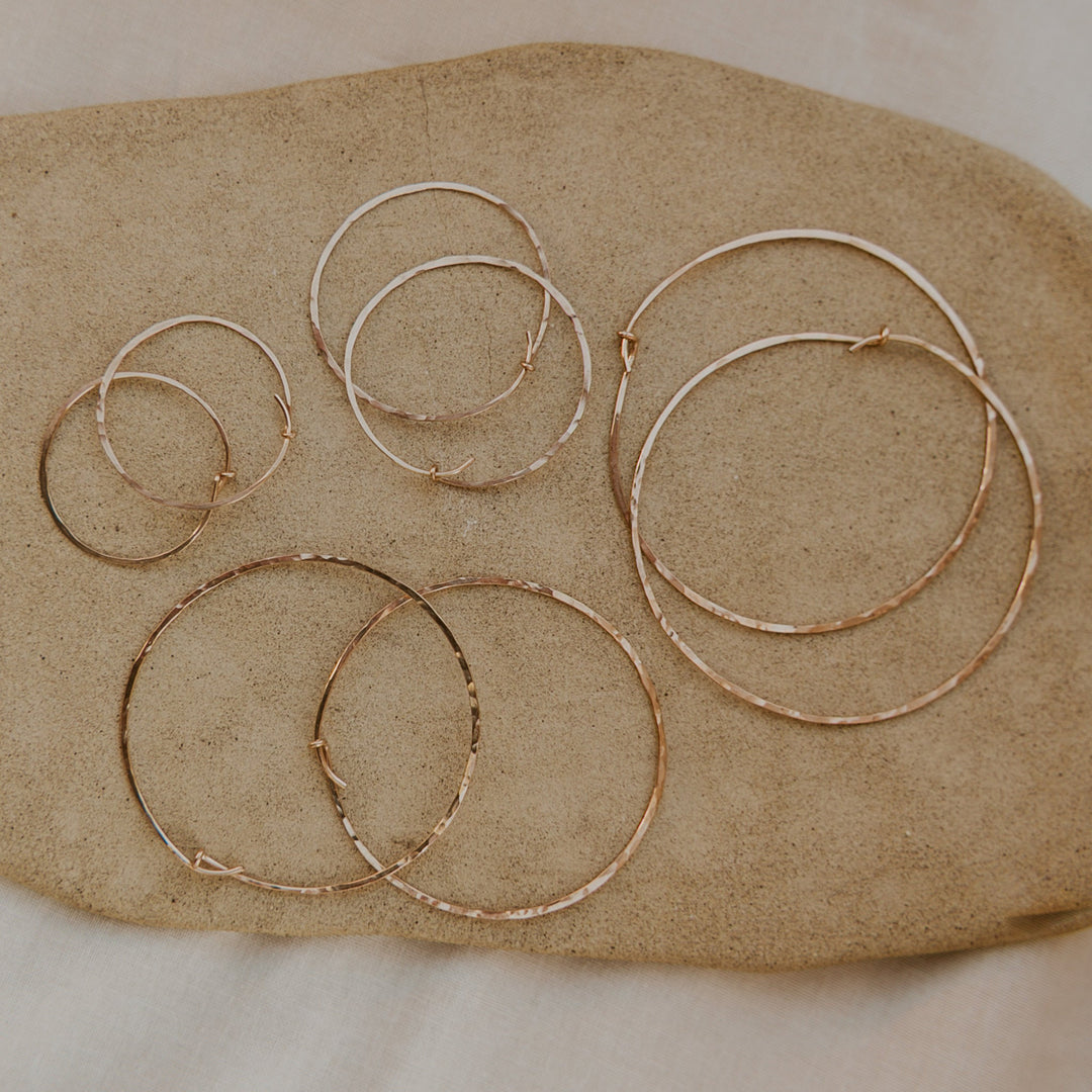 Set of gold hoop earrings on a beige stone surface