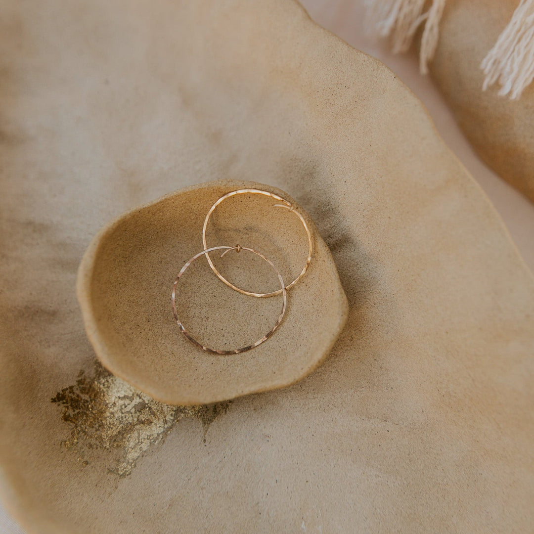 Two gold hoop earrings on a textured beige surface
