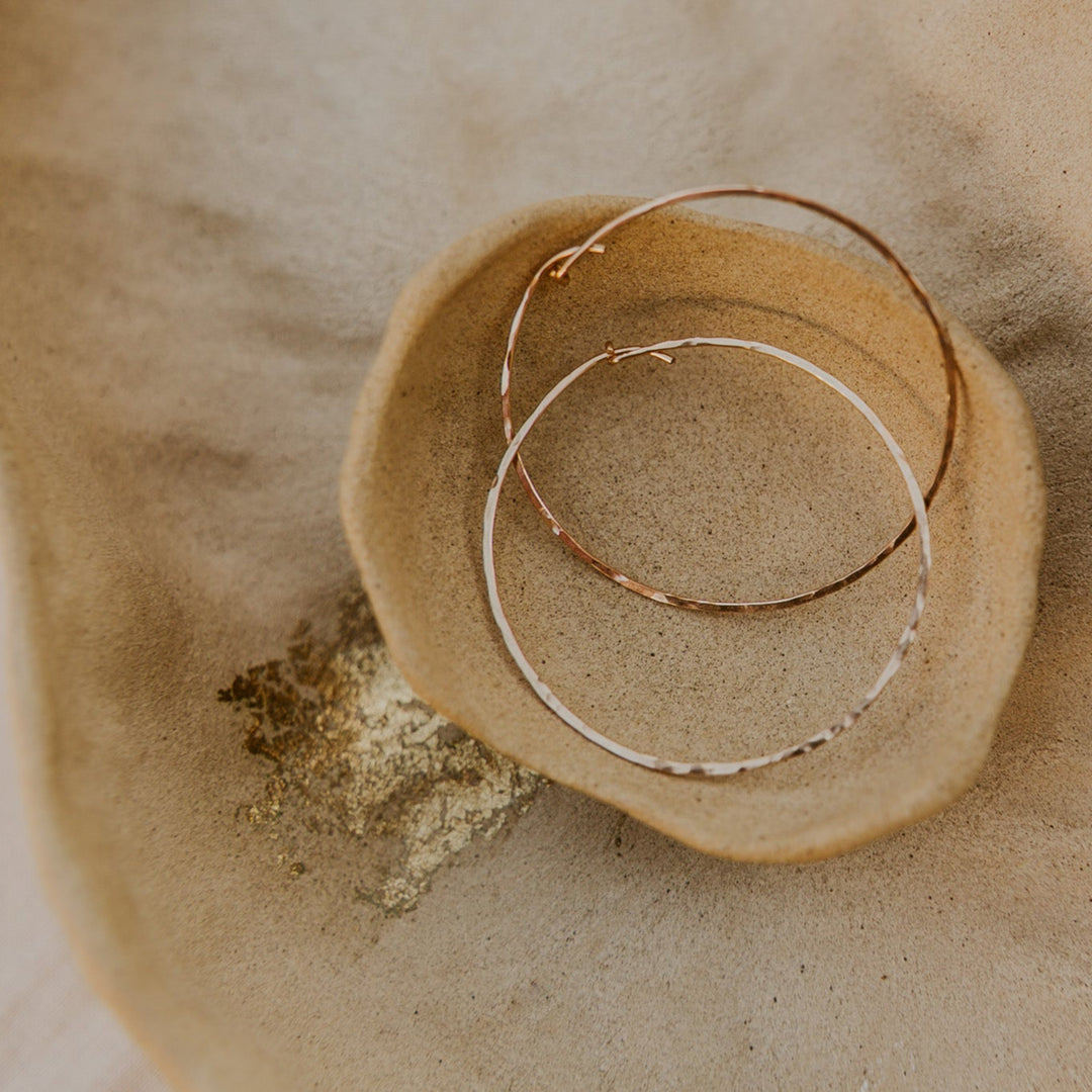 Two gold hoop earrings on a textured beige surface