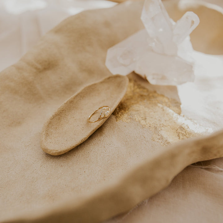 Close-up of a gold ring on a beige surface with a white object in the background