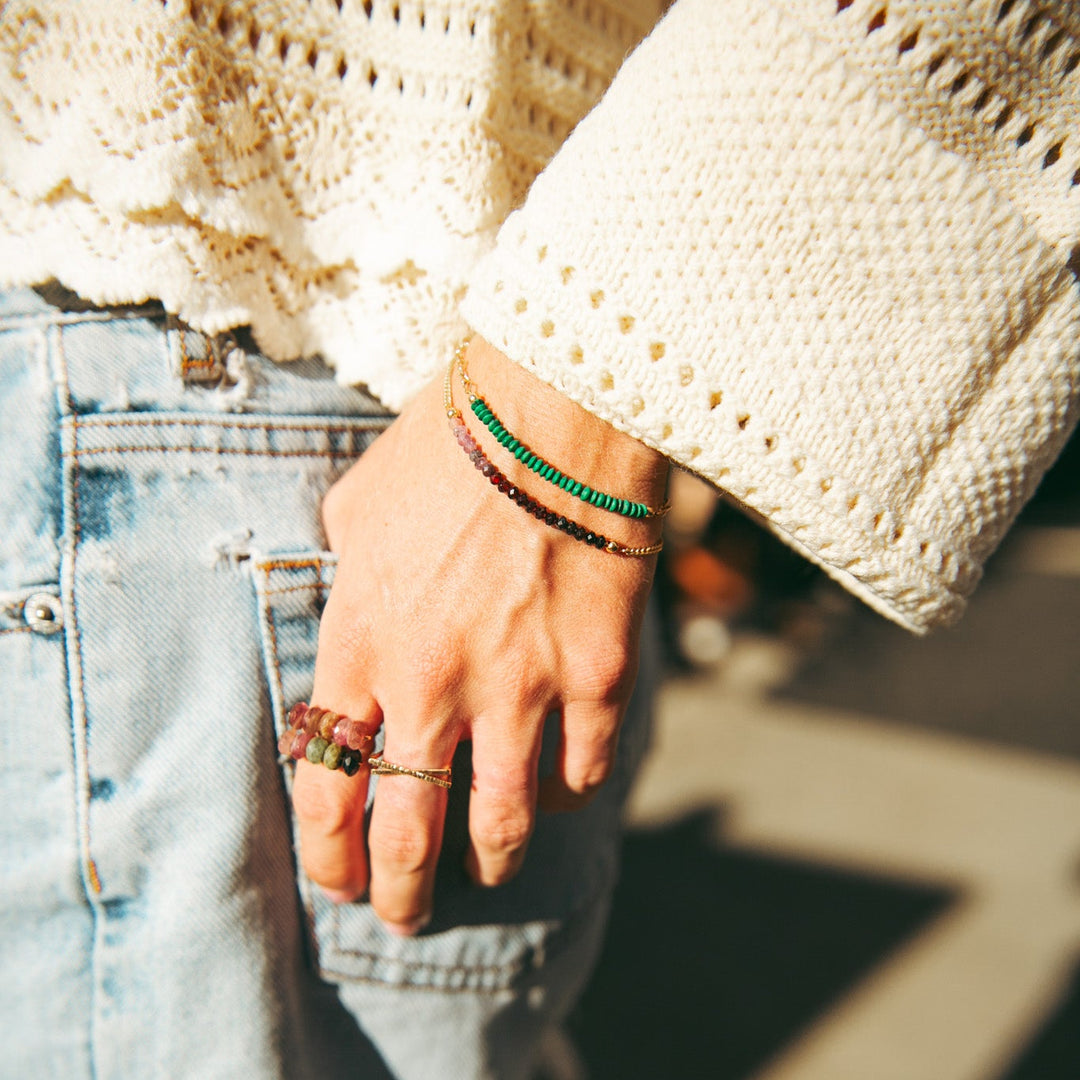 Close-up of a person's hand wearing bracelets and rings, with a blurred background.