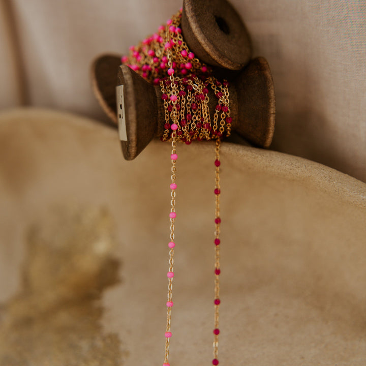 Gold and pink beaded chain on a wooden spool against a beige background