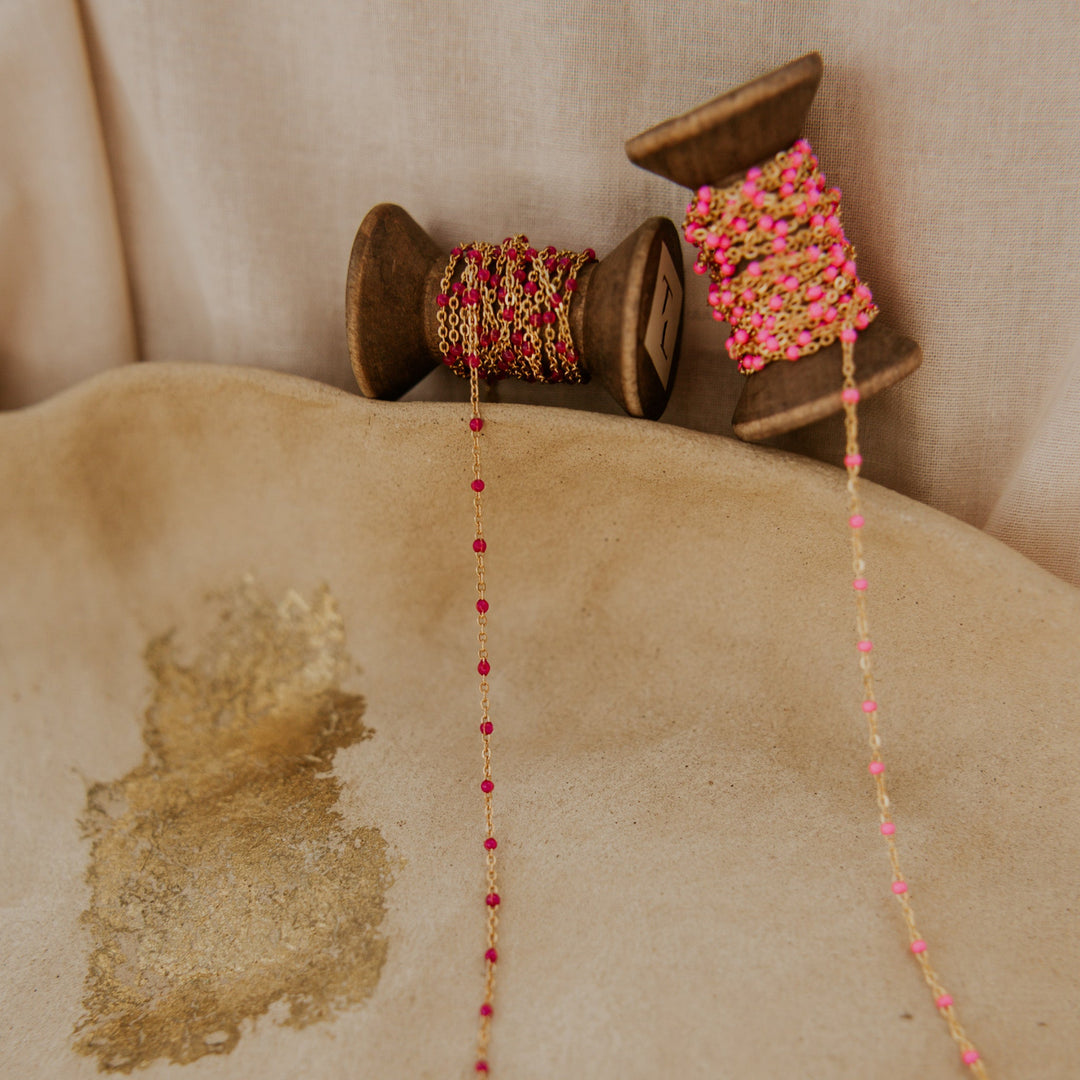 Decorative string with pink and gold beads on a wooden spool against a beige background