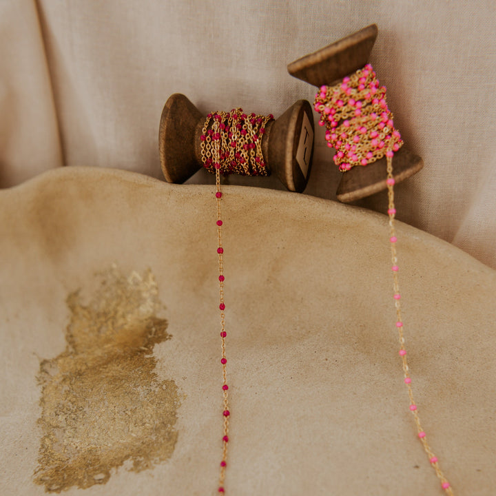 Decorative string with pink and gold beads on a wooden spool against a beige background