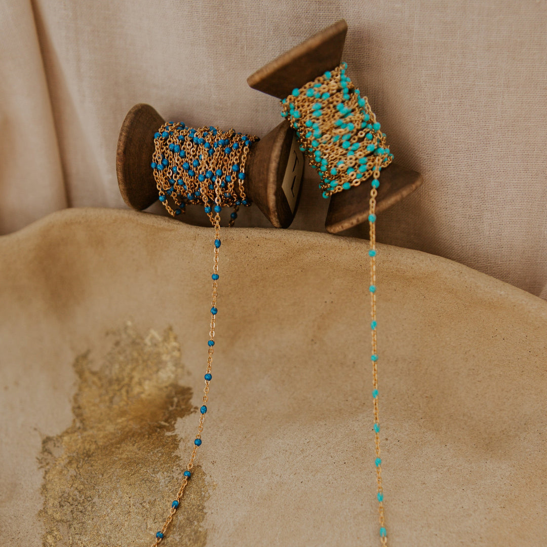 Gold and turquoise beaded necklace on a wooden spool against a beige background