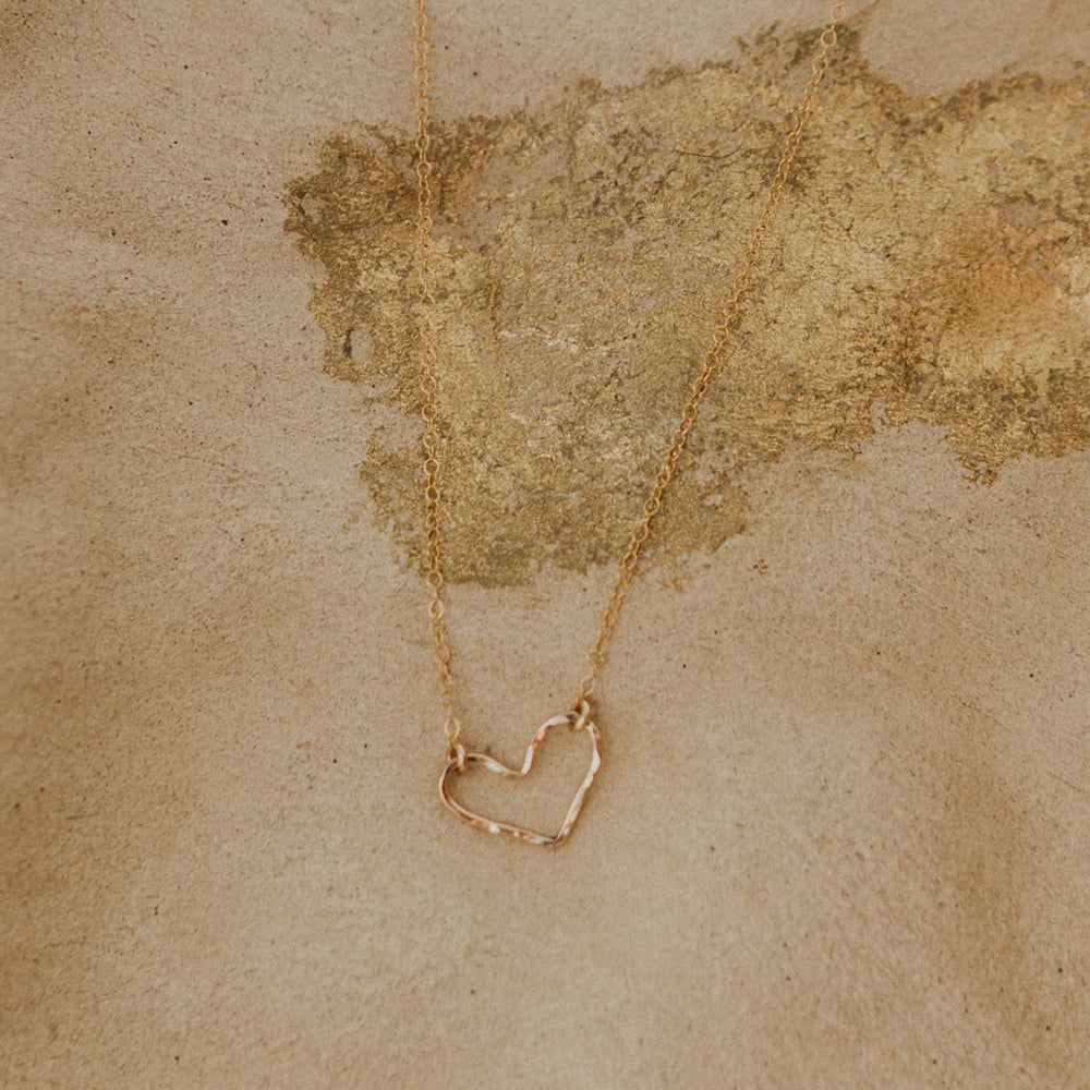 Gold necklace with a heart-shaped pendant on a textured beige background