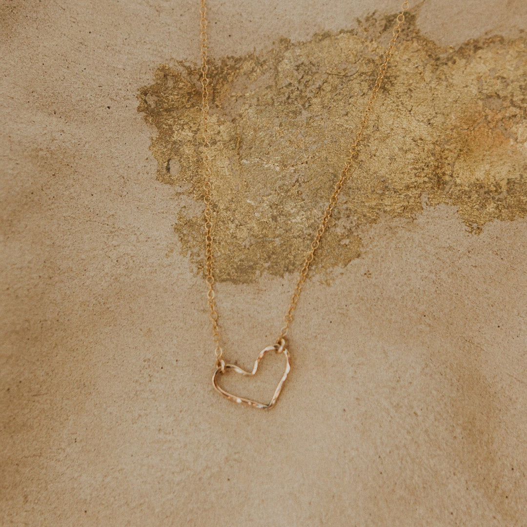 Gold necklace with a heart-shaped pendant on a textured beige background