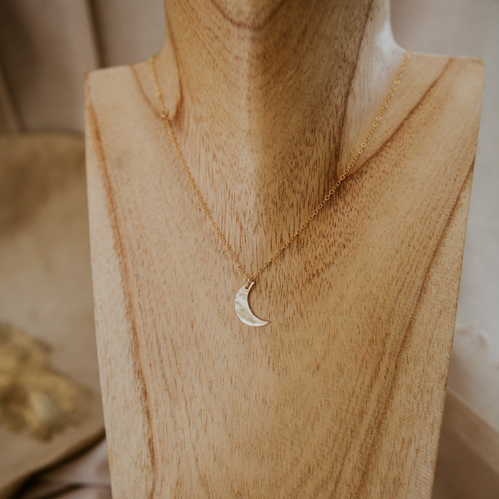 Gold necklace with a moon pendant on a wooden mannequin bust.