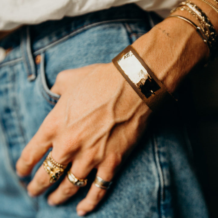 Close-up of a person's hand wearing gold rings and bracelets on blue jeans.