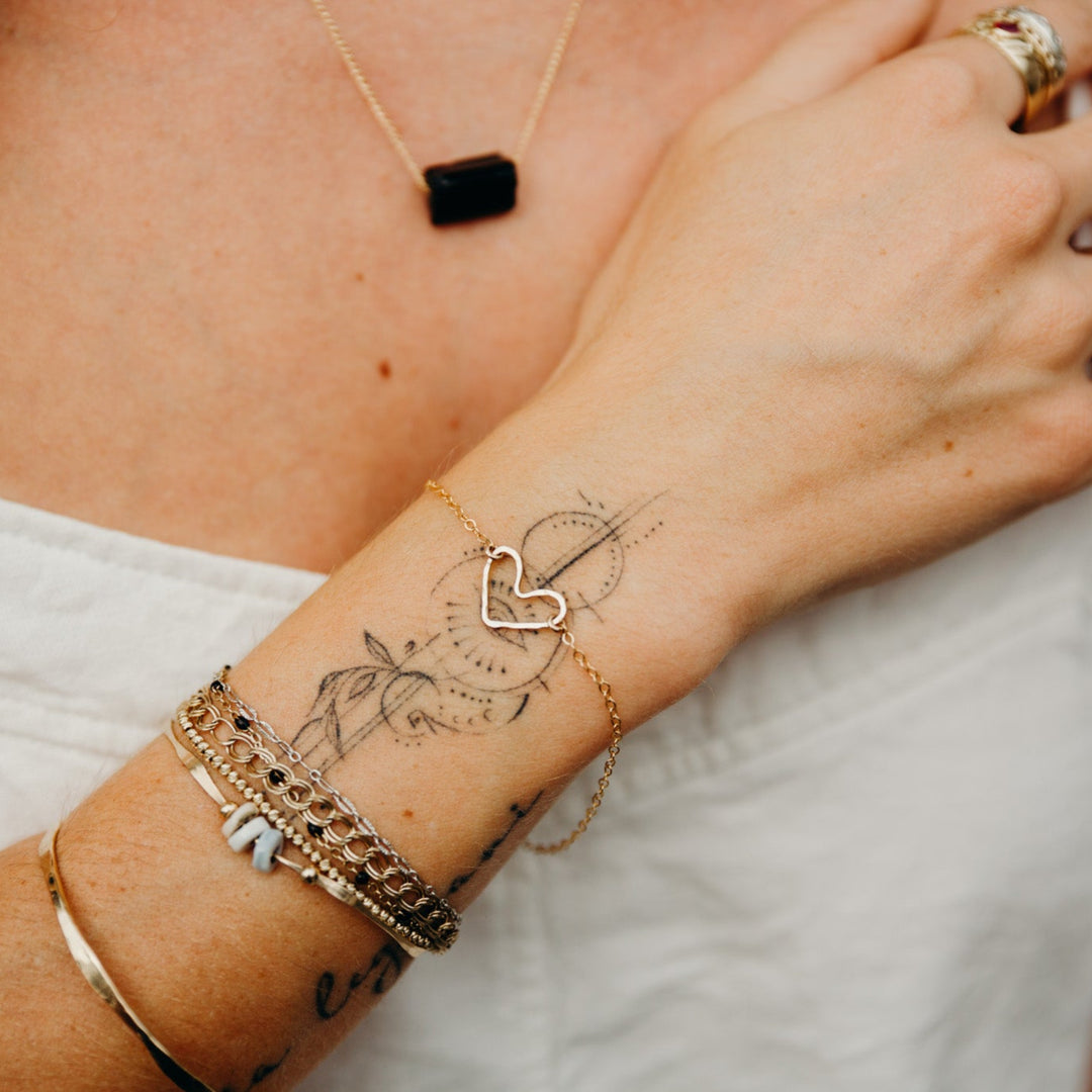 Close-up of a person's arm with tattoos, gold bracelets, and rings.