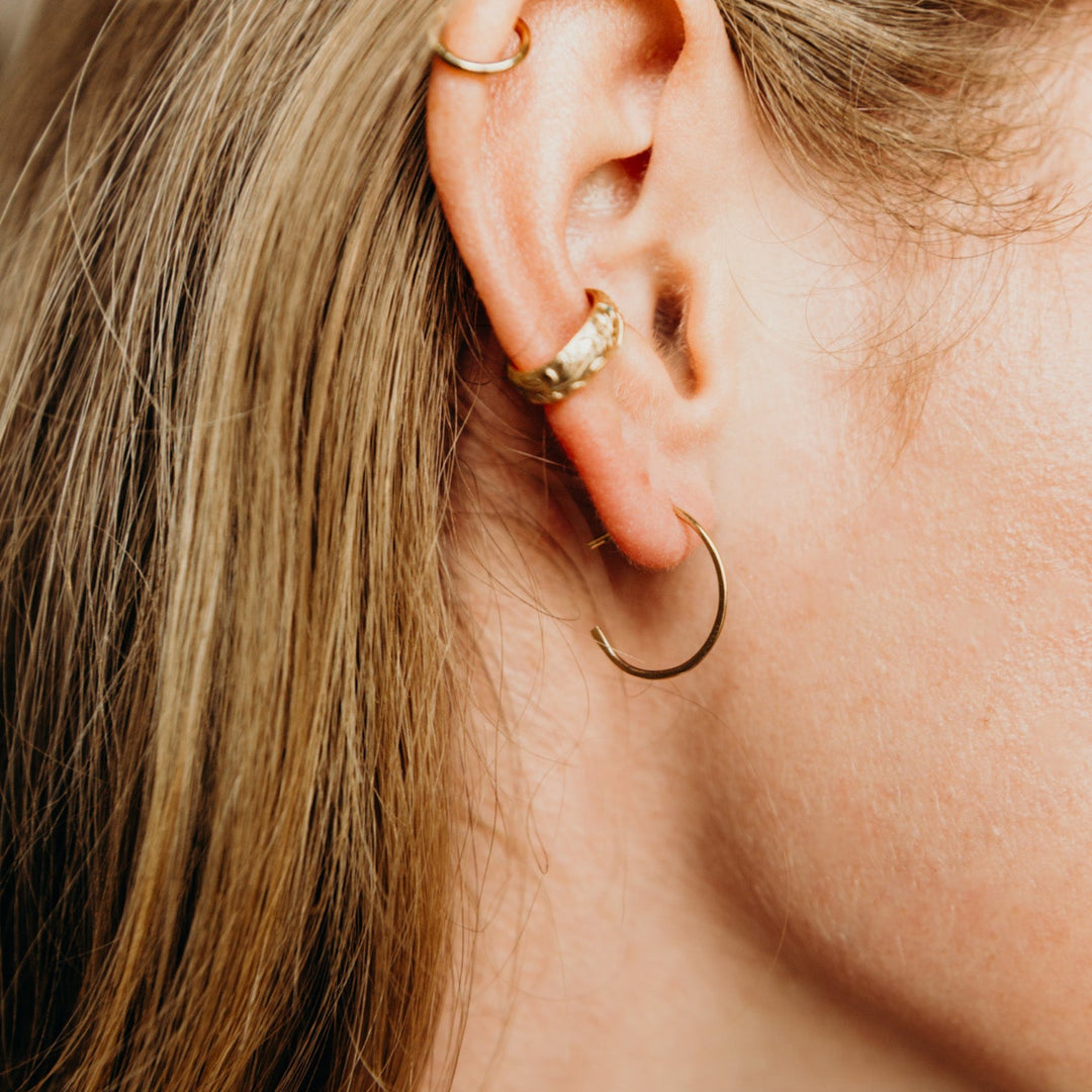 Close-up of an ear with gold hoop earrings and a gold earring.