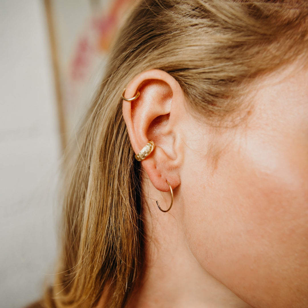Close-up of an ear with gold hoop earrings and a blurred background