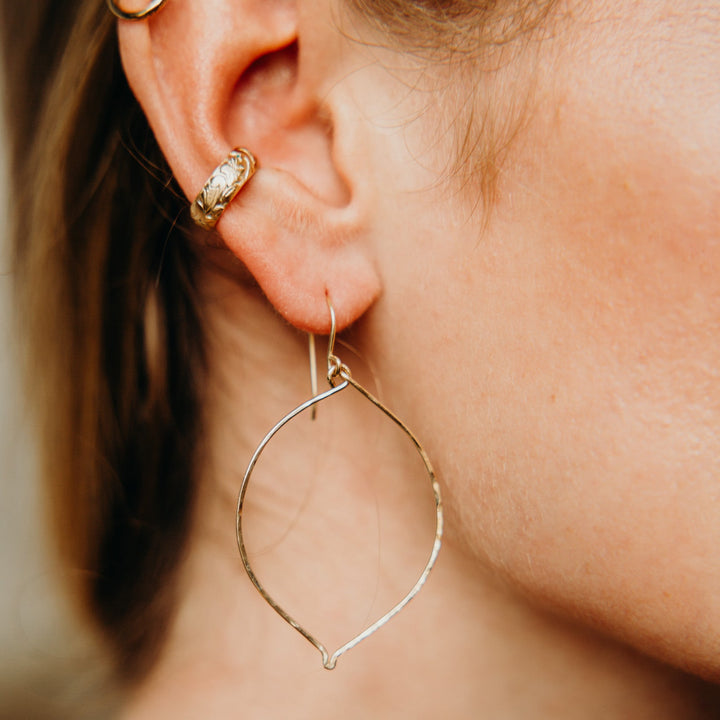 Close-up of a person wearing gold hoop earrings with a blurred background
