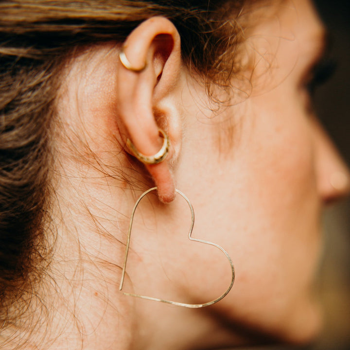 Close-up of a person wearing a heart-shaped earring with a blurred background