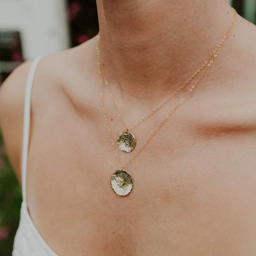 Close-up of a person wearing two gold necklaces with circular pendants.