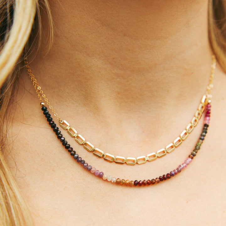 Model wearing the Aurora Necklace with multi-color spinel gemstones on gold chain layered with other necklaces.
