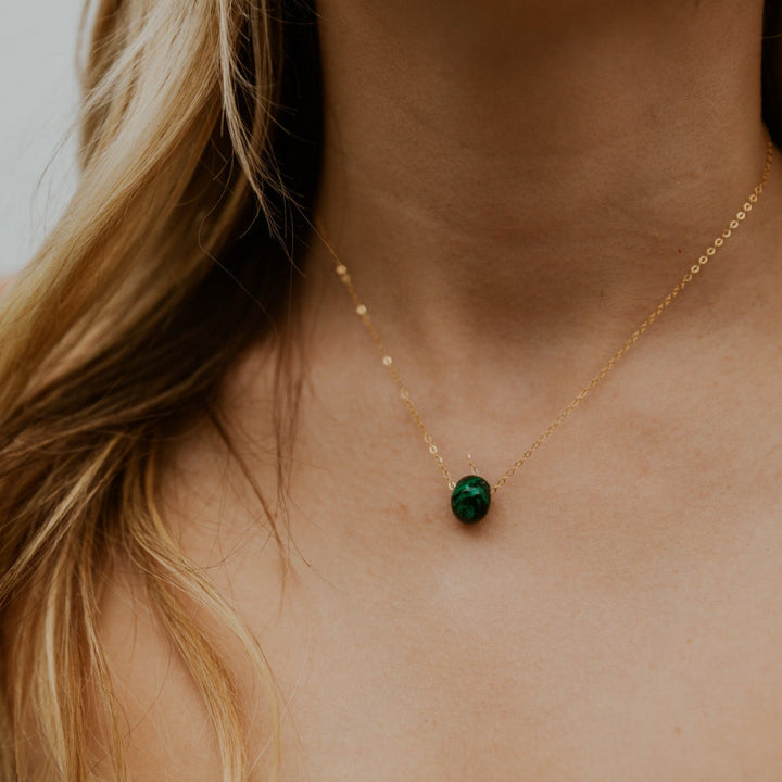 Gold necklace with a green gemstone pendant on a person with blonde hair.