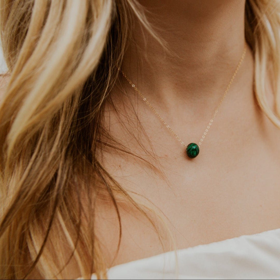 Close-up of a person wearing a delicate necklace with a green pendant.