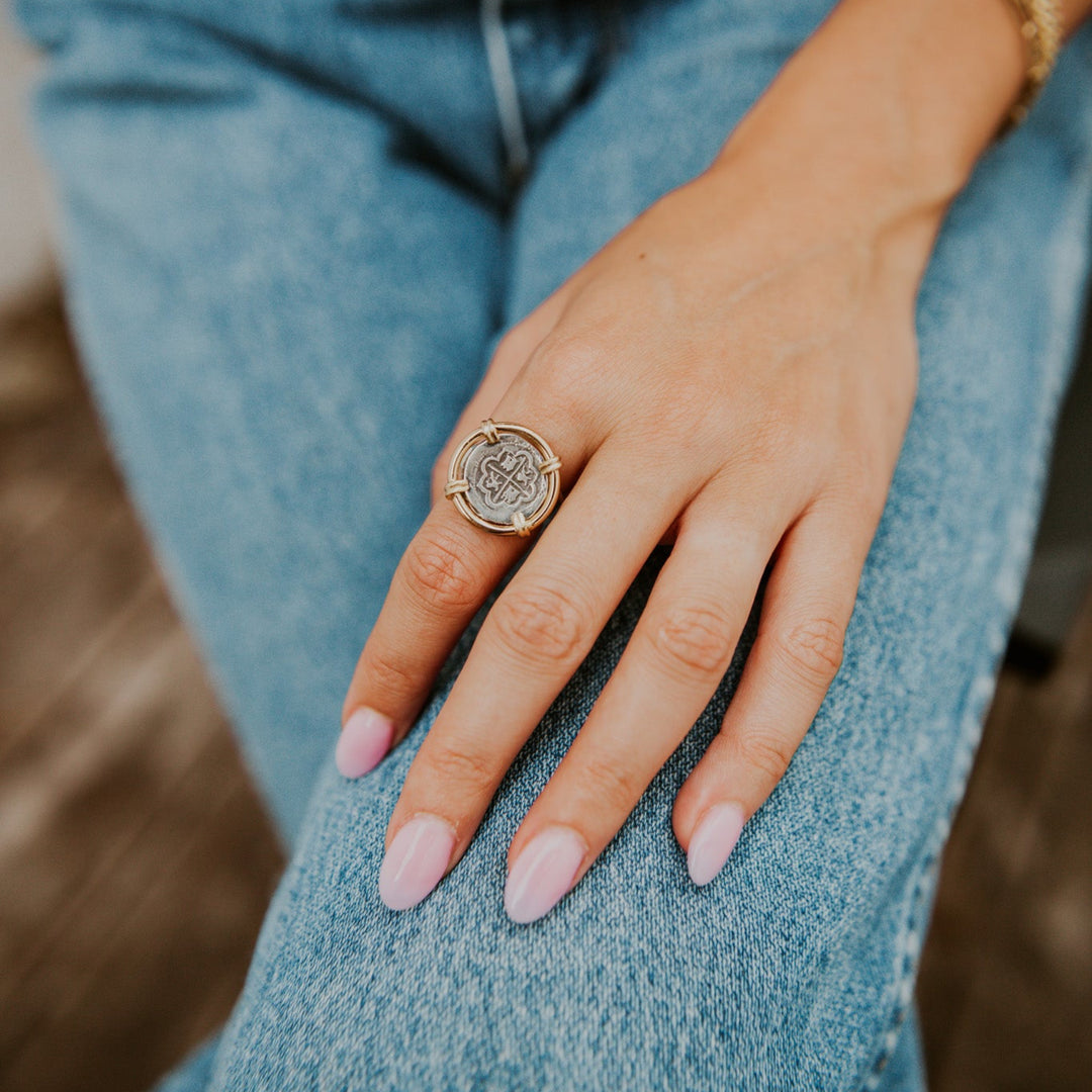 Close-up of a hand wearing a decorative coin ring with blue jeans in the background