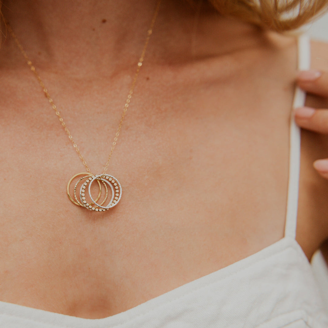 Gold necklace with circular pendants on a person wearing a white top.