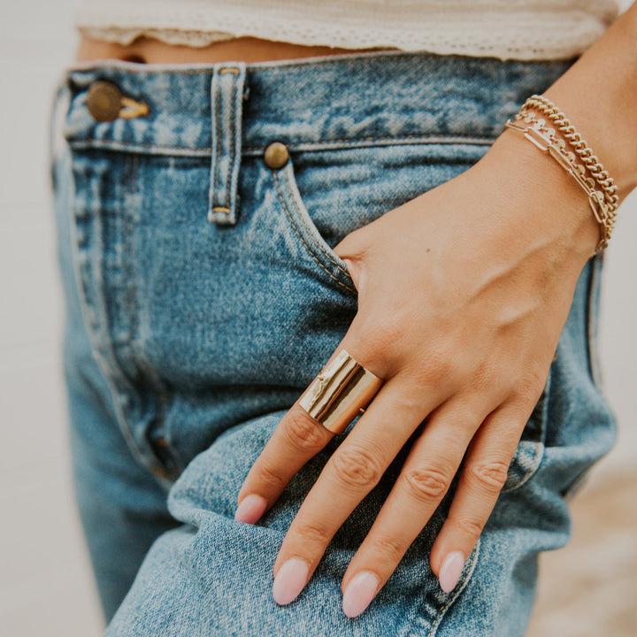 Person wearing blue jeans and a beige top with a gold ring and bracelet.