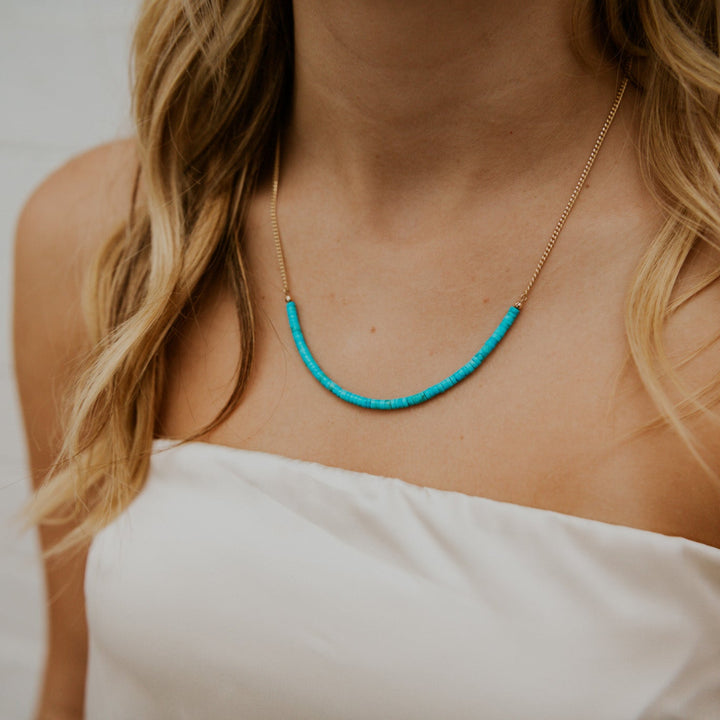 Person wearing a turquoise necklace with a white garment