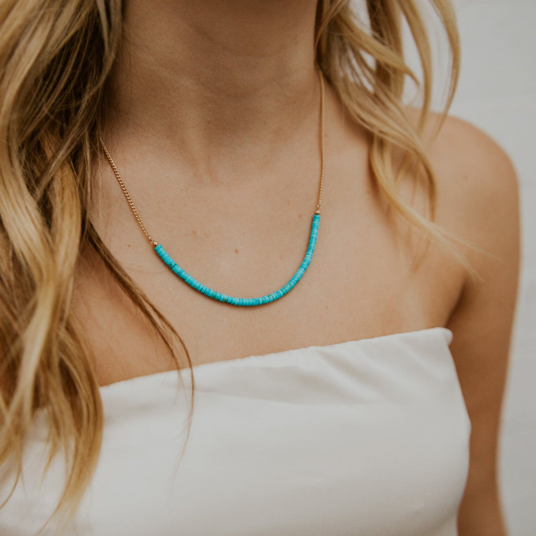 Person wearing a turquoise beaded necklace with a plain background