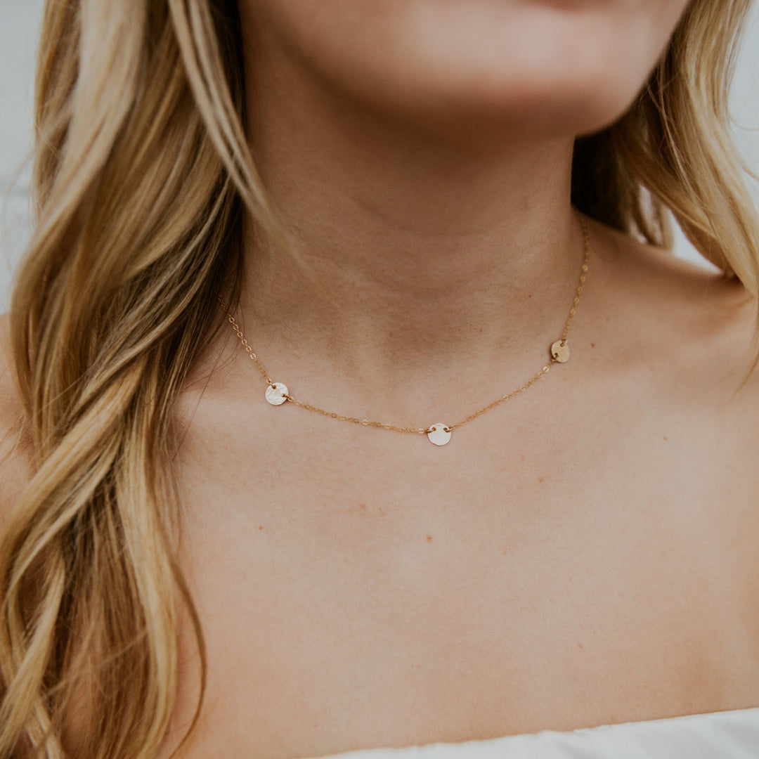 Close-up of a person wearing a delicate gold necklace with small round pendants.
