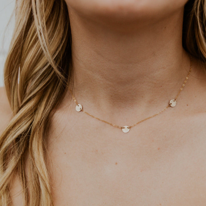 Close-up of a person wearing a delicate gold necklace with small round pendants against a neutral background.