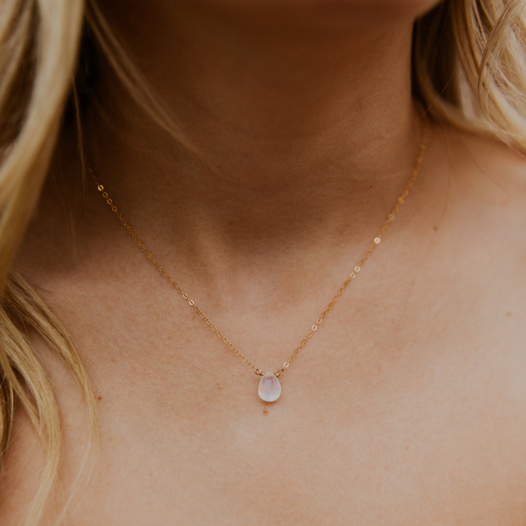 Gold necklace with a teardrop-shaped pendant on a person's neck