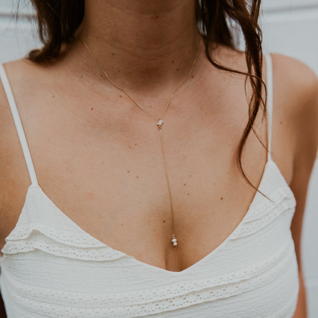 Close-up of a person wearing a delicate necklace with a white top.