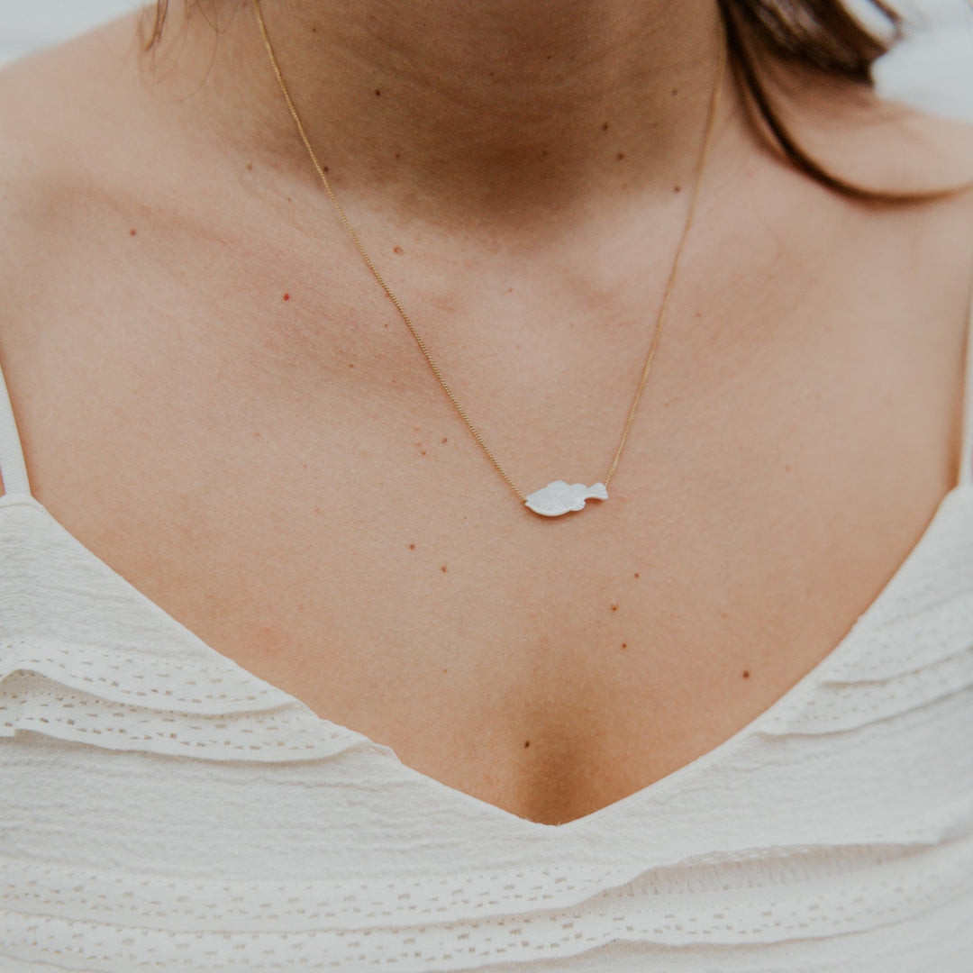 Close-up of a person wearing a delicate necklace with a white top.