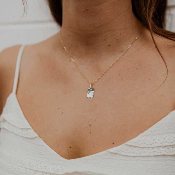 Necklace with a pendant worn by a person in a white top against a neutral background