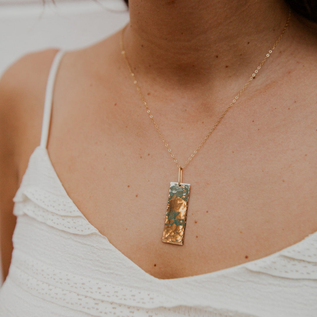 Necklace with a rectangular pendant worn by a person in a white top.