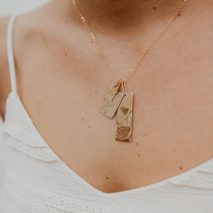 Gold necklace with two pendants on a person wearing a white top.