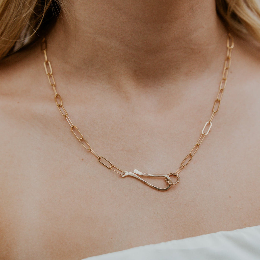 Gold chain necklace with a unique clasp on a person's neck
