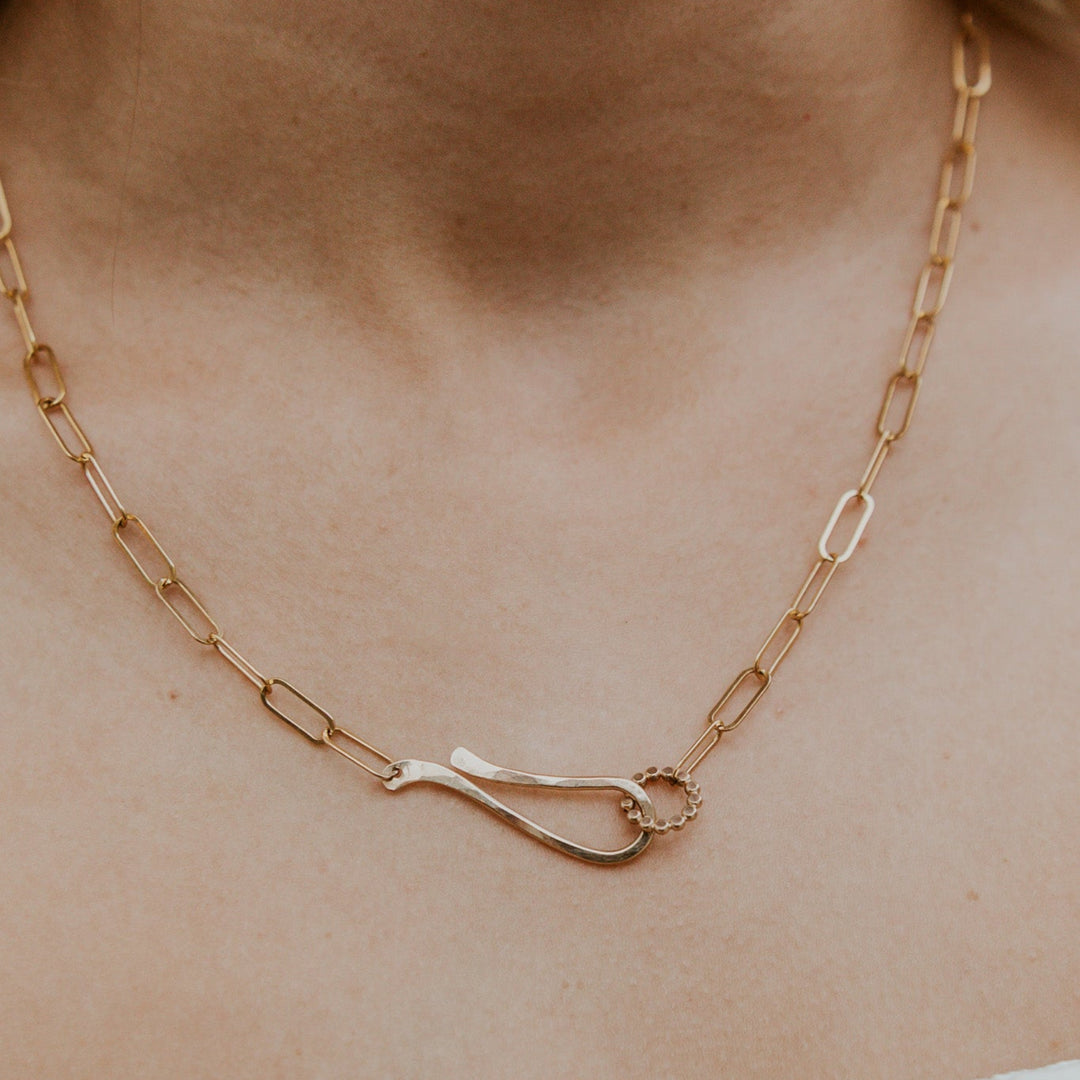 Gold chain necklace with a unique clasp on a person's neck