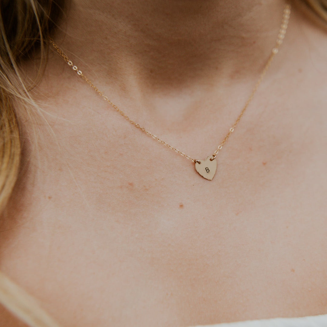 Close-up of a gold necklace with a heart pendant on a person's neck.