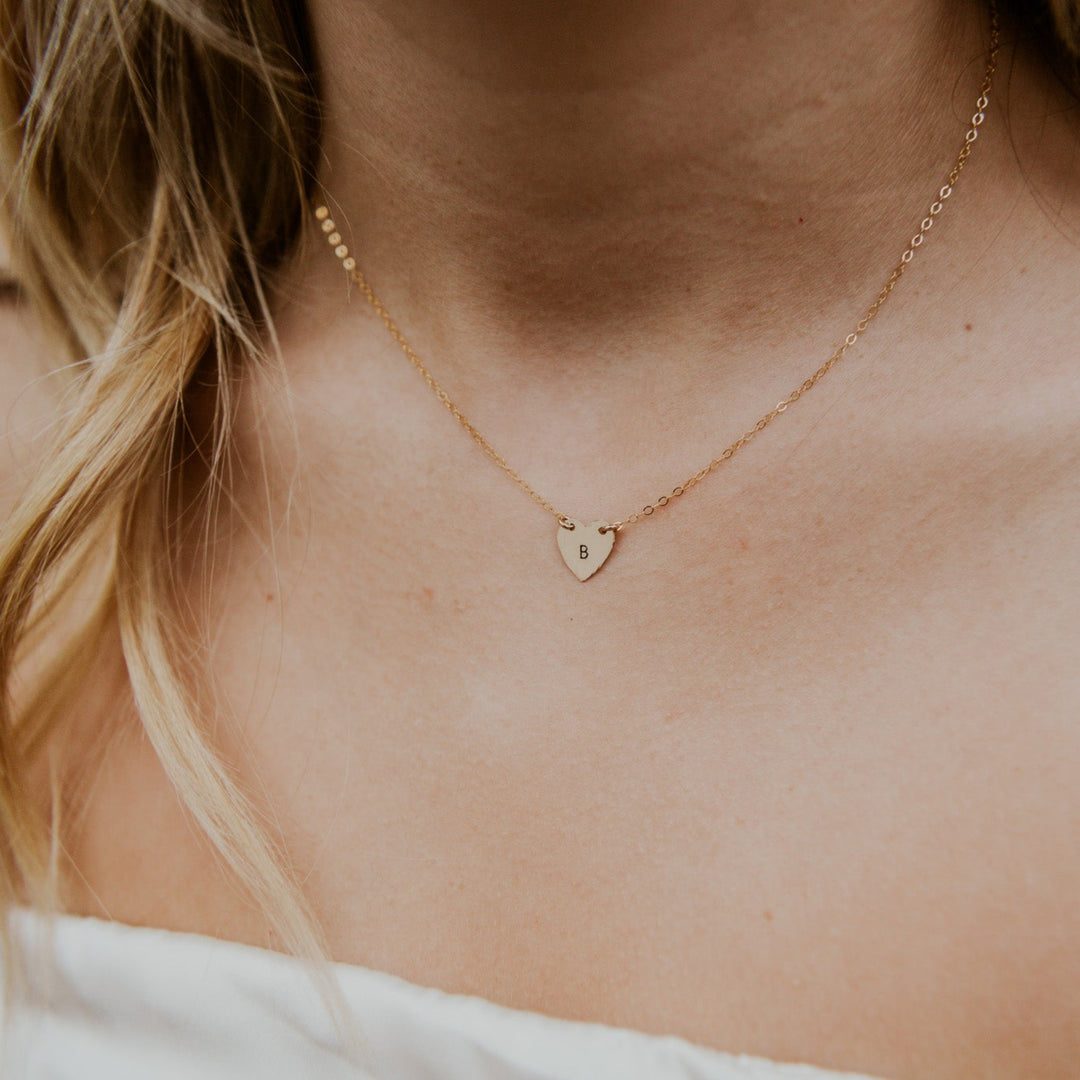 Close-up of a person wearing a gold necklace with a heart pendant.