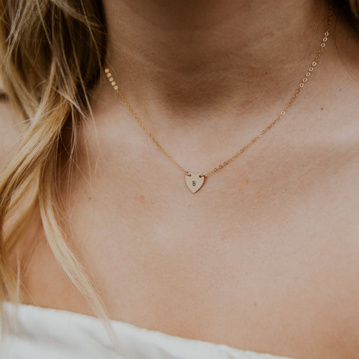 Close-up of a person wearing a gold necklace with a heart pendant.