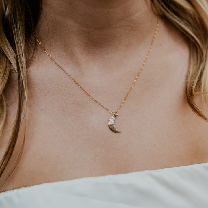 Gold necklace with a moon pendant on a person's neck