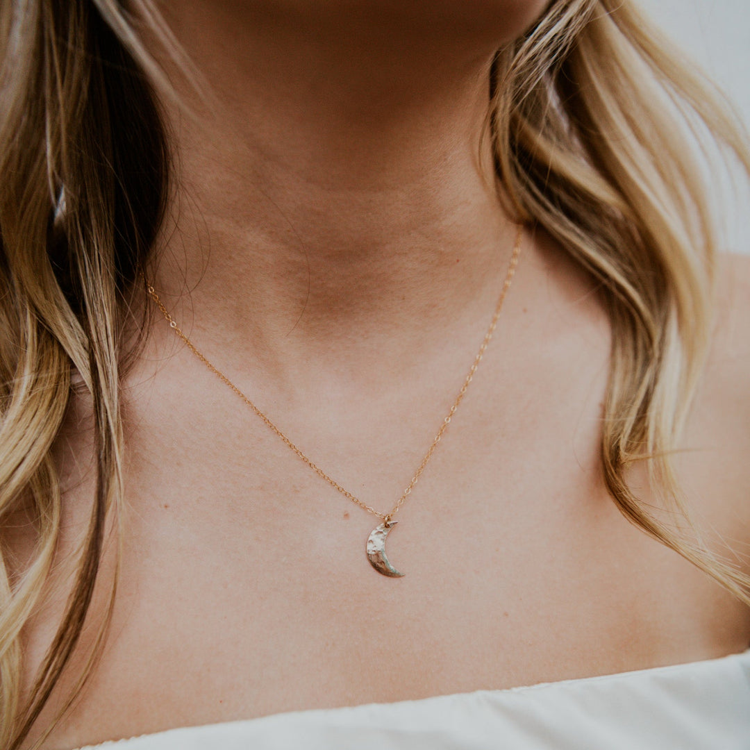 Gold necklace with a moon pendant worn by a person with blonde hair.