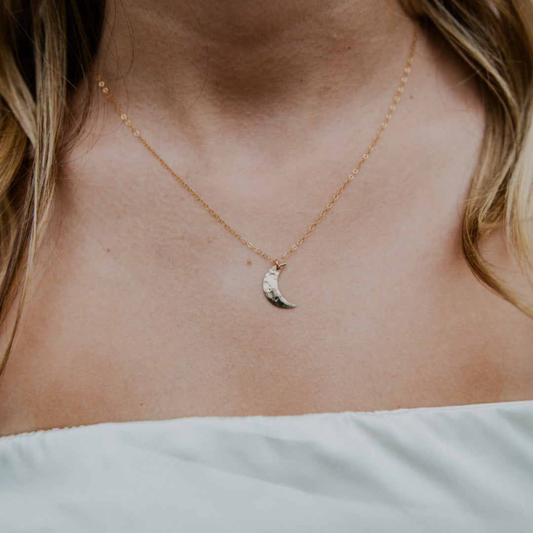 Close-up of a person wearing a delicate gold necklace with a small pendant.