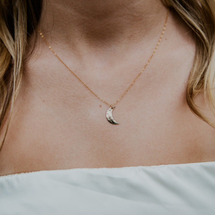 Close-up of a person wearing a delicate gold necklace with a small pendant.