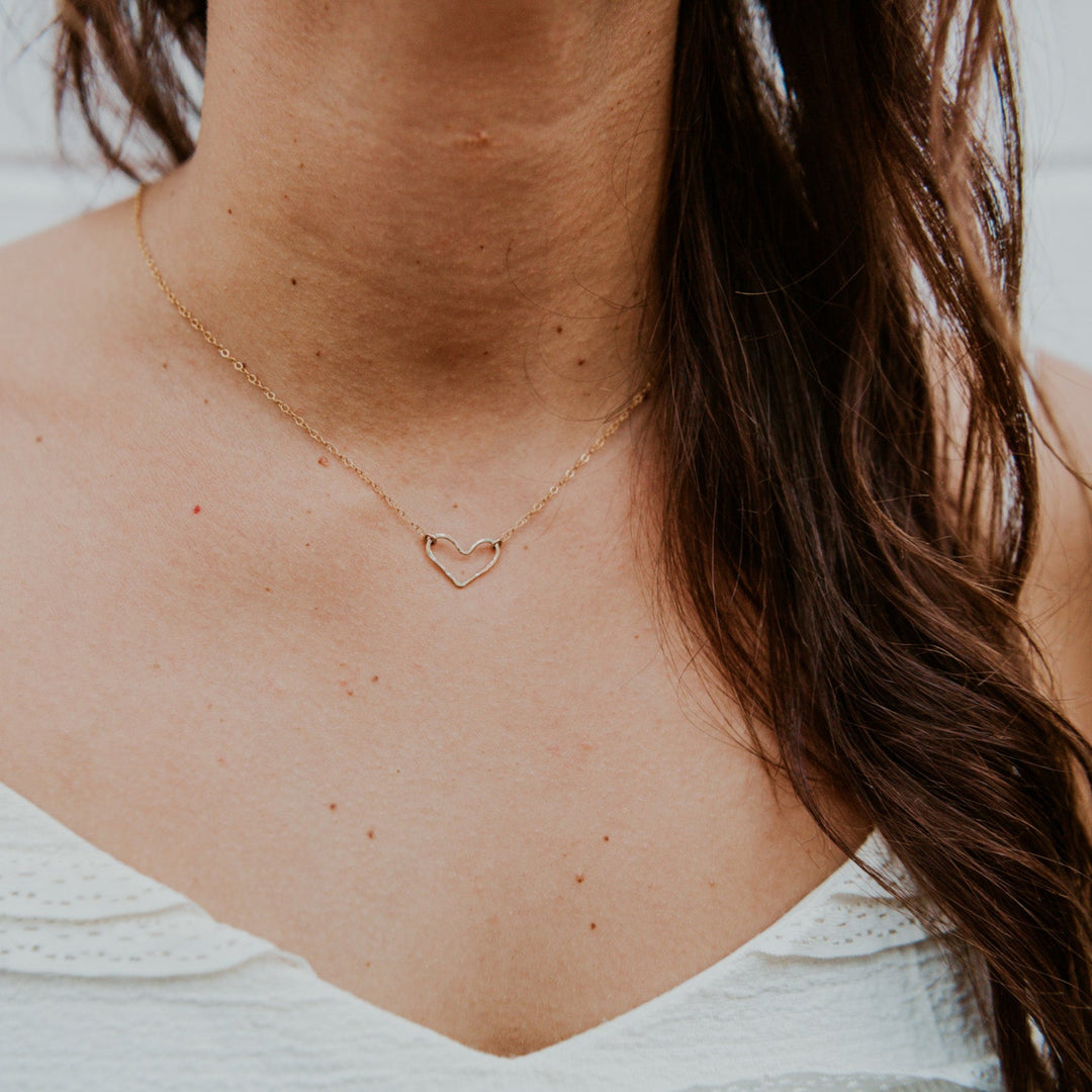 Close-up of a person wearing a delicate necklace with a heart pendant against a neutral background